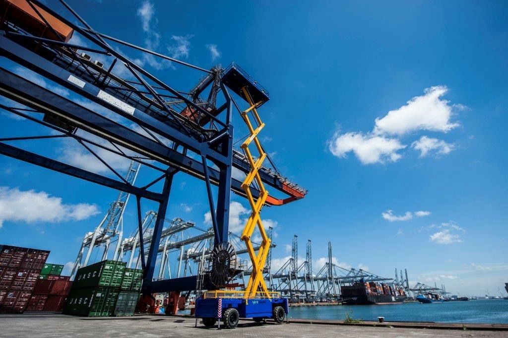 Yellow lift near large blue crane at a port with blue sky and scattered clouds.