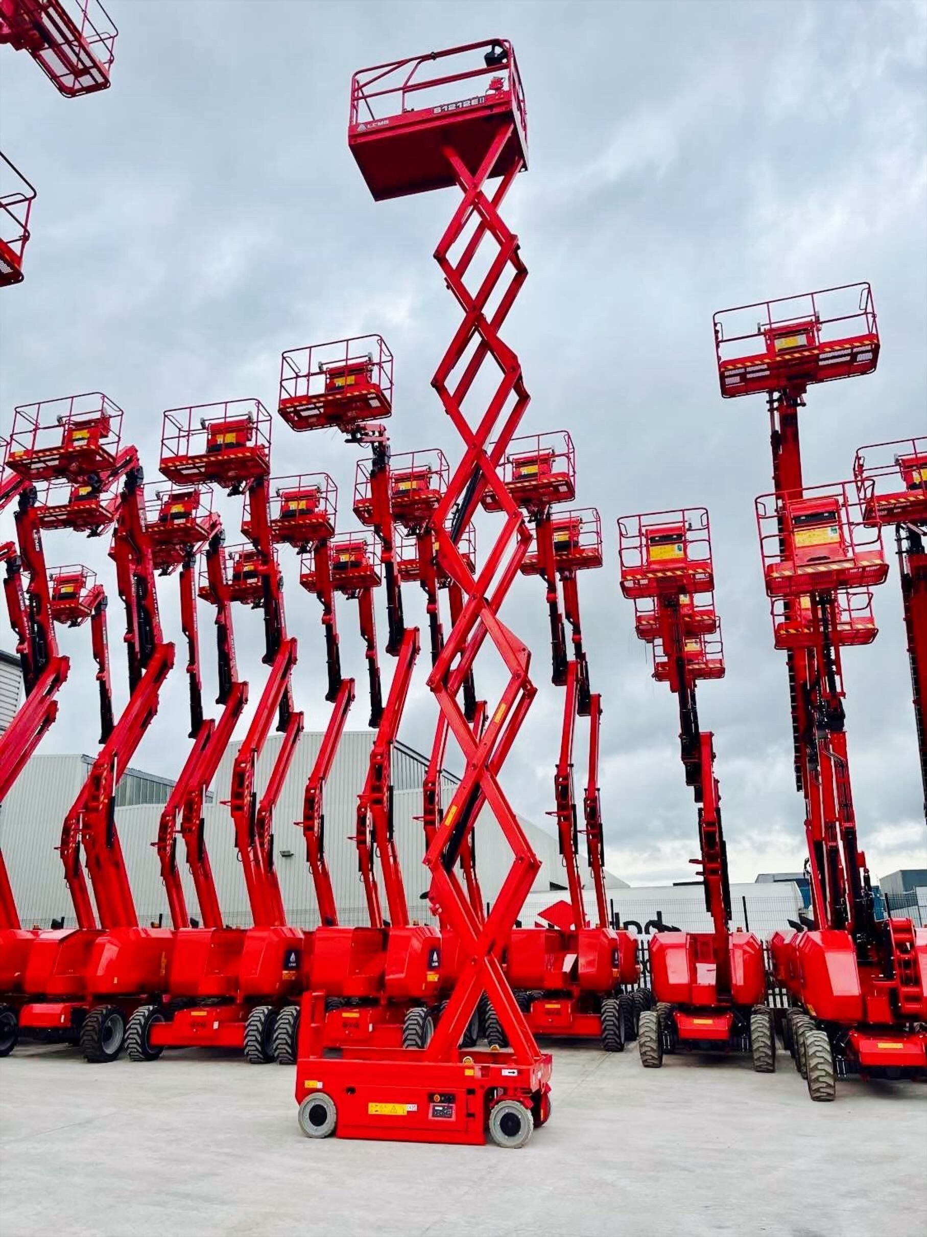 Red scissor lifts, many in a row, with one fully extended against a cloudy sky.