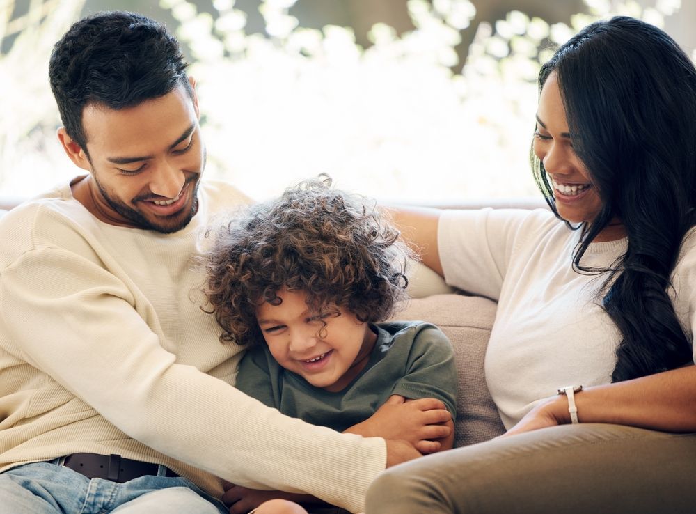 Smiling family sitting together on a couch, cuddling a young child in a bright living room