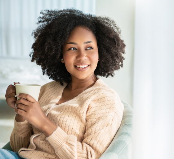 Smiling person in a cream sweater holding a mug on a bright couch