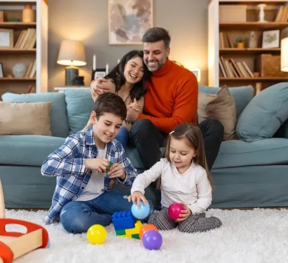 Family playing with colorful toys on a living room carpet in front of a blue couch