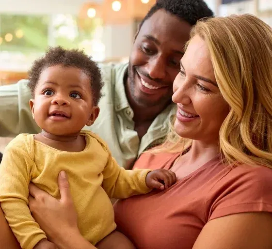 Smiling couple holding a baby in a warm indoor setting