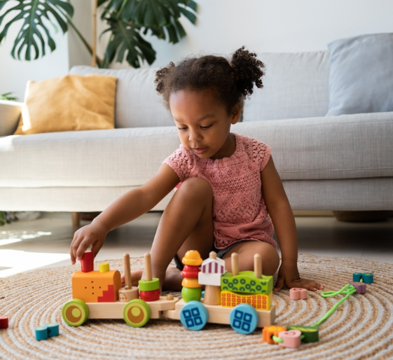 Child playing with colorful toy train on a rug in a living room