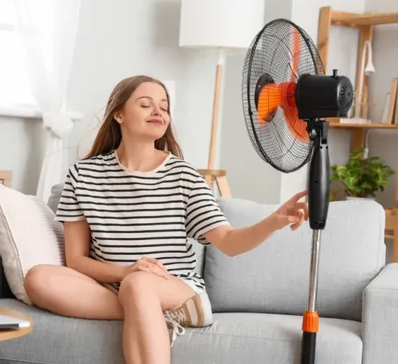 Woman sitting on a sofa reaching toward an orange-bladed fan in a bright living room
