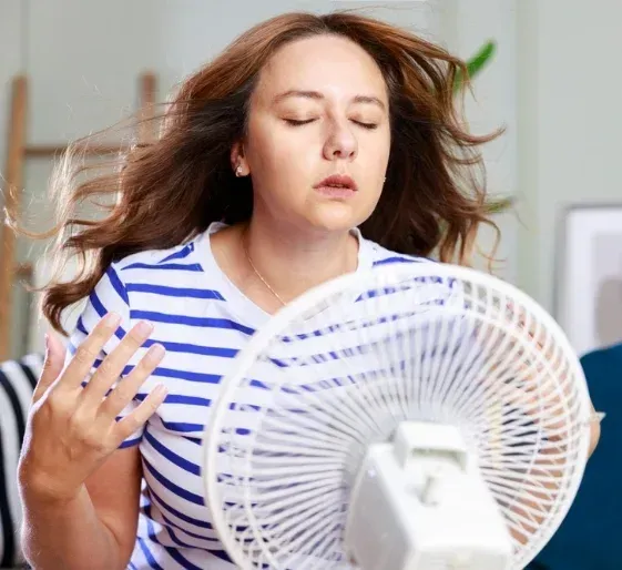 Person fanning themselves with a desk fan, looking overheated in a striped shirt