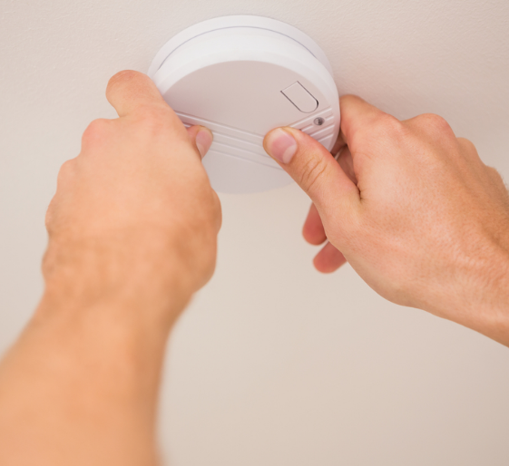 Hands installing a white smoke detector on a ceiling