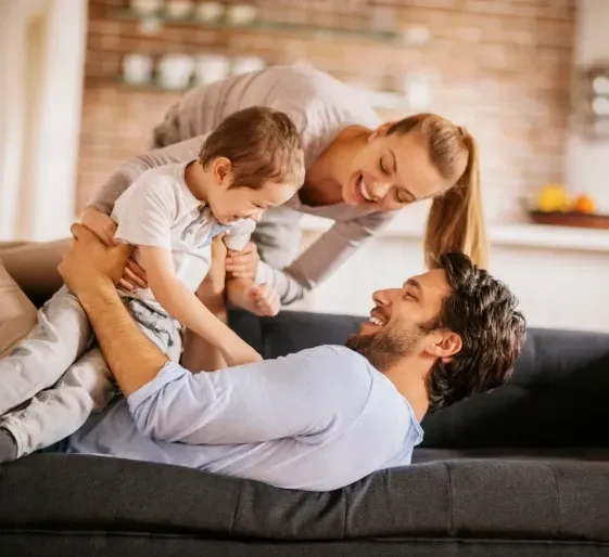Family cuddling on a couch in a cozy living room, smiling and embracing.