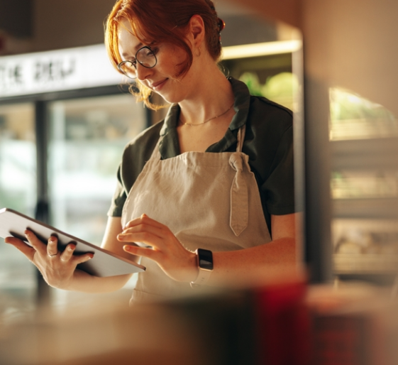 Barista in an apron taps a tablet in a warmly lit café.