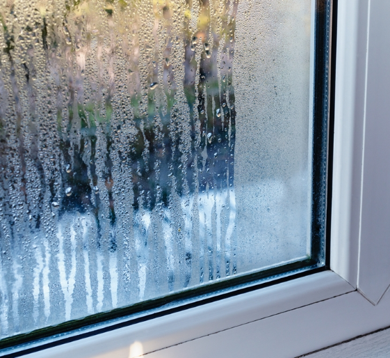 Fogged window with condensation droplets and a blurry outdoor view beyond the glass