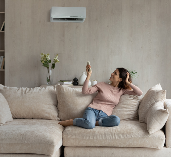Person reclining on a beige sofa, holding a phone and looking up in a living room with an air conditioner.