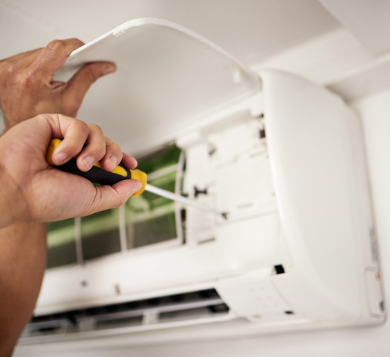 Hands using a screwdriver to clean an open wall-mounted air conditioner