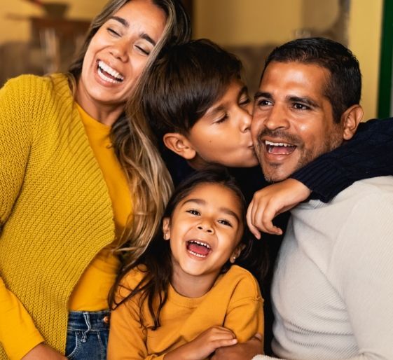 Smiling family hugging indoors, wearing warm yellow and white sweaters