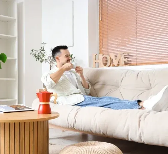 Person lounging on a white sofa in a bright living room with a coffee cup and orange table lamp