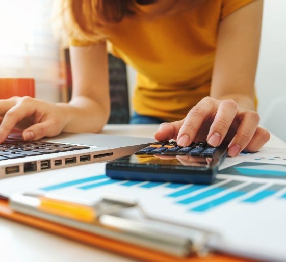 Person using a laptop and calculator over printed charts on a desk