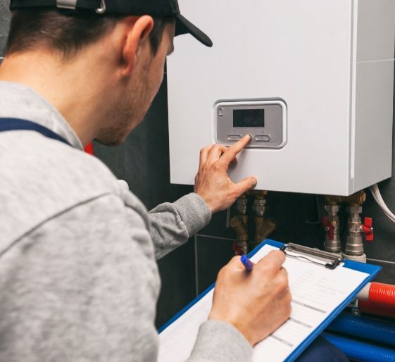 Technician inspecting a wall-mounted boiler while writing on a clipboard in a utility room