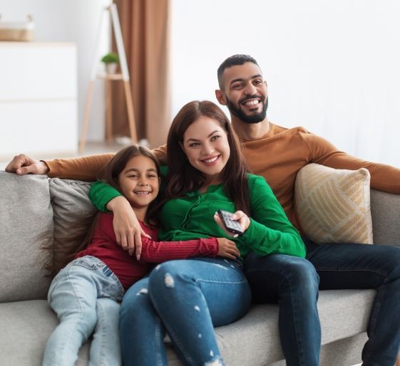 Smiling family of three sitting on a couch, embracing in a bright living room.