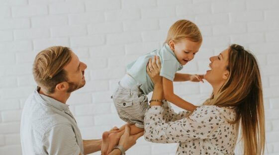 Family lifting smiling toddler in a bright white room