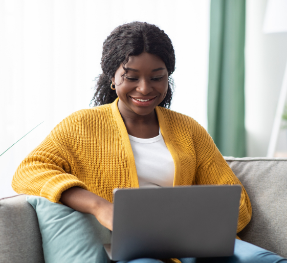 Smiling person in a yellow sweater using a laptop on a couch