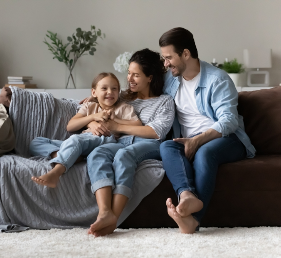 Three people sitting on a couch, smiling and cuddling in a cozy living room