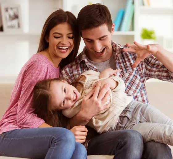 Smiling family on a couch, parents hugging a laughing child in a cozy living room