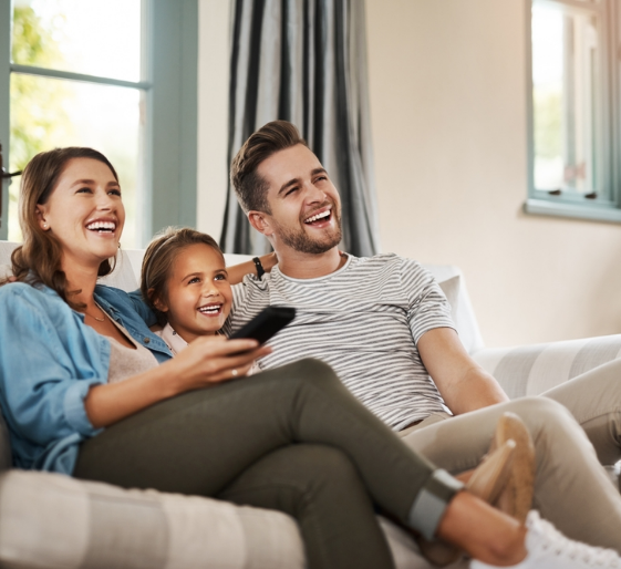 Smiling family on a couch watching TV together in a bright living room