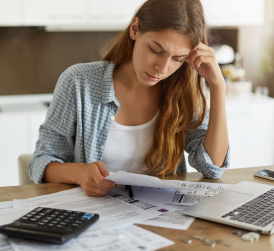Woman reviewing bills at a desk with calculator and laptop, looking concerned.