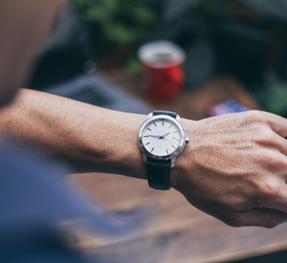 Close-up of a wrist wearing a silver watch with a black strap, outdoors with a blurred background