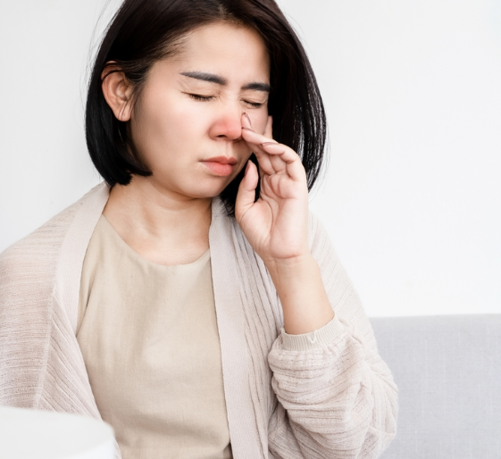 Woman holding her nose and grimacing on a couch, suggesting discomfort or nausea