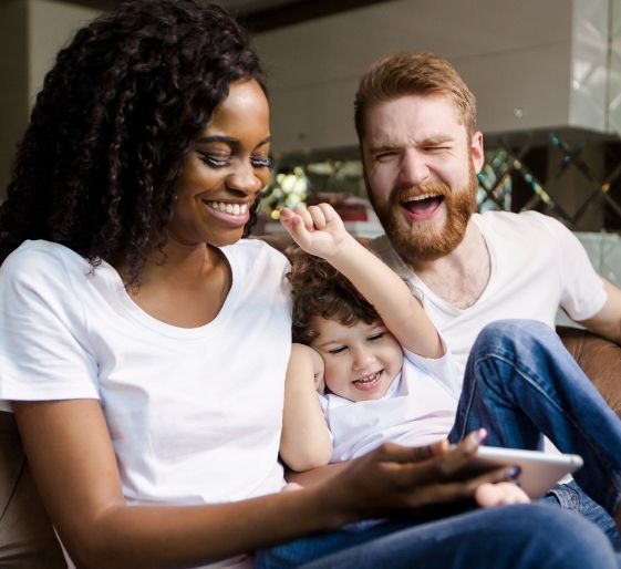 Three people smiling on a couch, looking at a phone together