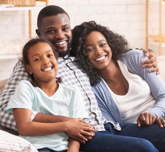 Three smiling people sitting on a couch in a bright living room