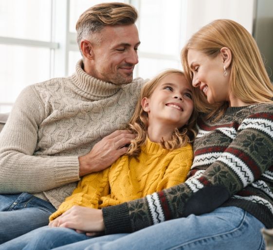 Family of three cuddling on a couch, smiling in warm sweaters in a cozy living room
