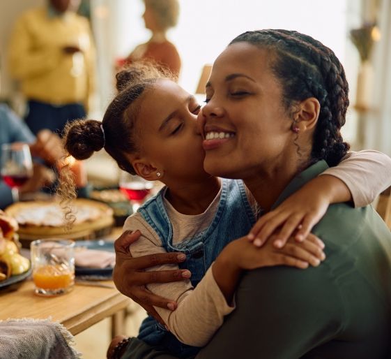 Child hugging smiling adult at a dining table during a warm family meal
