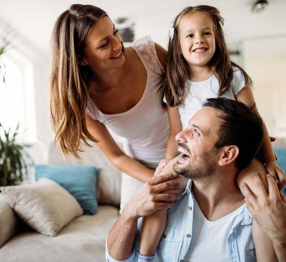 Smiling family in a bright living room, mother and child leaning over a seated father