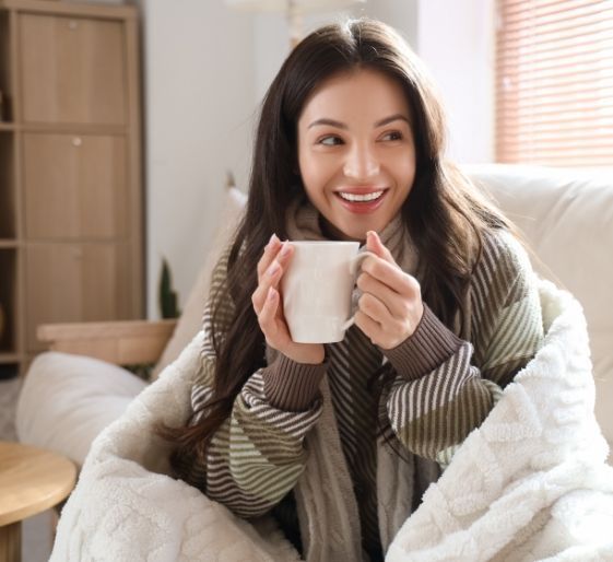 Woman smiling on a cozy couch, holding a white mug in a bright living room.