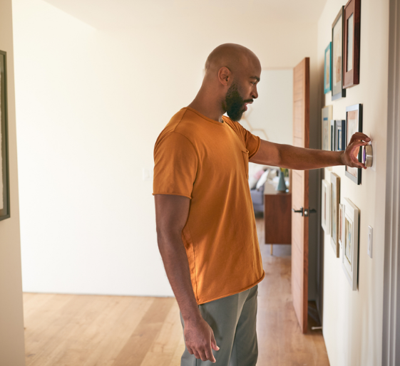 Man in orange shirt unlocking a white wall-mounted device in a bright hallway