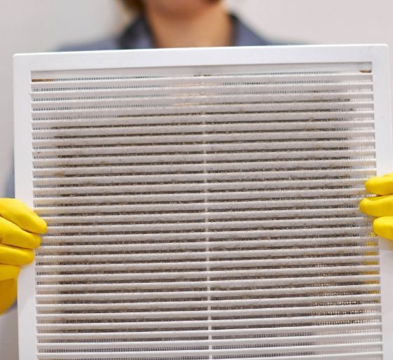 Person in yellow gloves holding a dirty air filter at chest level