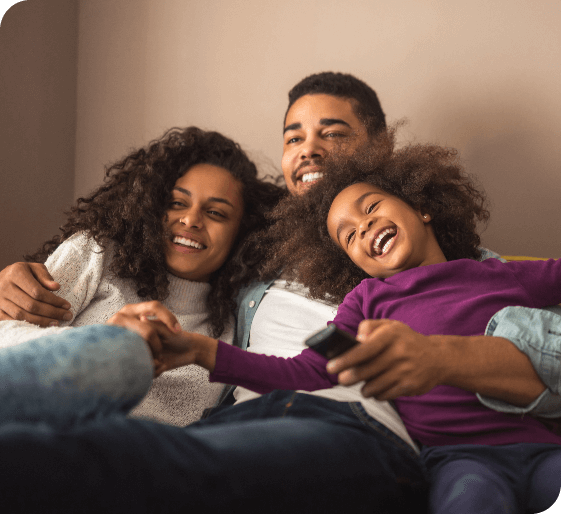 Three smiling people lounging together on a couch, embracing and laughing