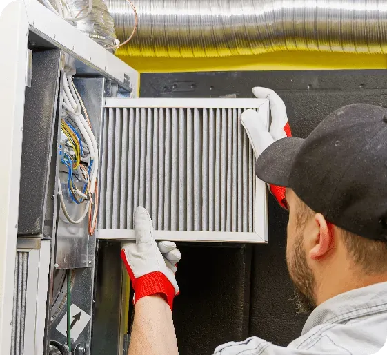 Worker installing HVAC filter in a duct system, wearing white gloves and a black cap.