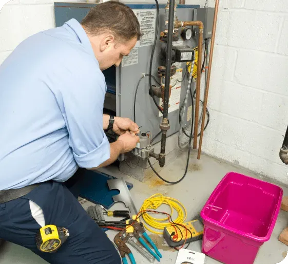 Technician kneeling beside a water heater, using tools and wires during repair work in a utility room