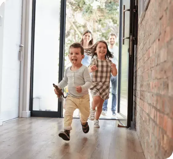 Children running indoors through an open doorway, smiling in a bright hallway