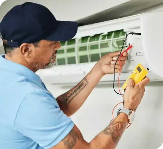 Technician testing wall-mounted air conditioner wiring with a multimeter