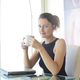 A woman is sitting at a desk drinking a cup of coffee