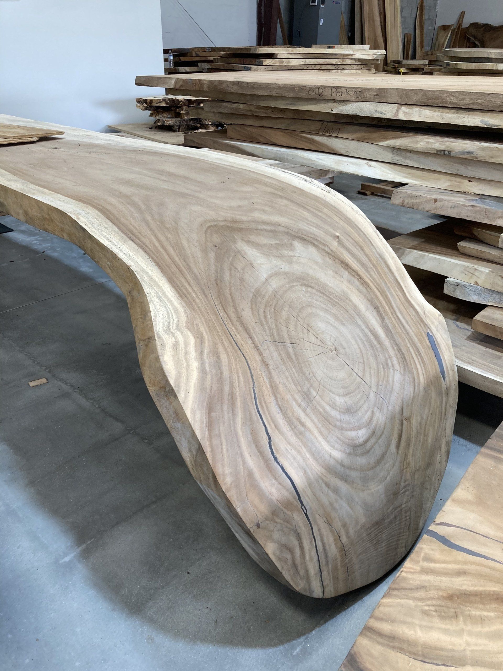 A large piece of wood is sitting on the floor next to a pile of wood.