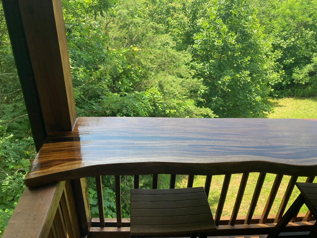 A balcony with a wooden table and chairs and trees in the background.