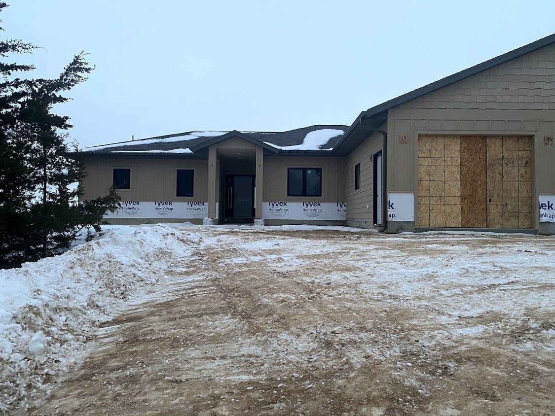 Snowy driveway leading to a beige house with a boarded-up garage door