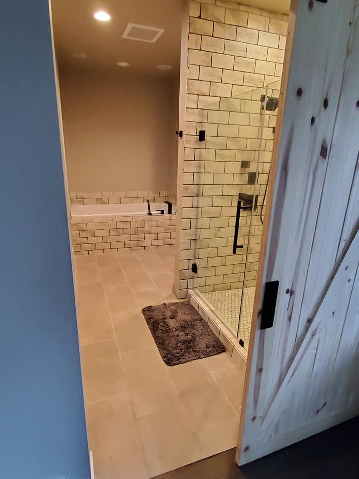 Modern bathroom with glass shower, beige tile, and a partially open wooden door