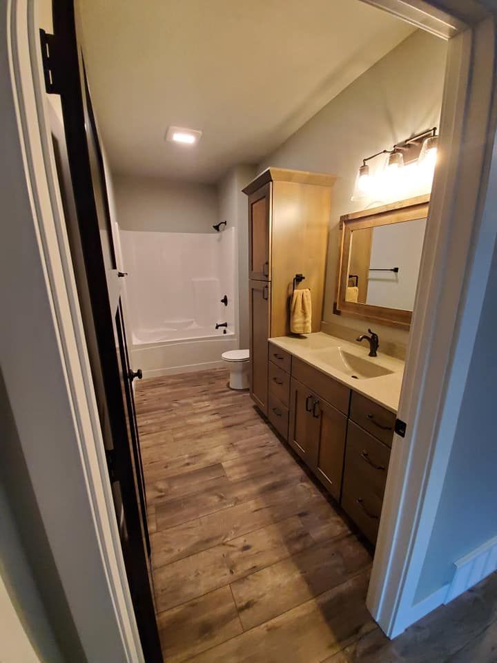 Bathroom with vanity, mirror, toilet, and bathtub; wood-look flooring and recessed ceiling light.