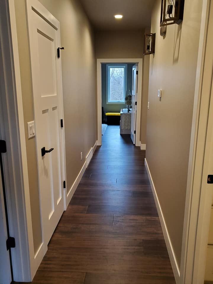 Narrow hallway with beige walls, dark wood floor, and a bright room at the end.