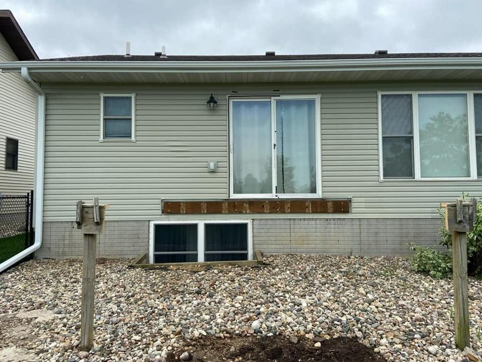 Back view of a gray house with sliding glass doors, windows, and a gravel yard with two posts