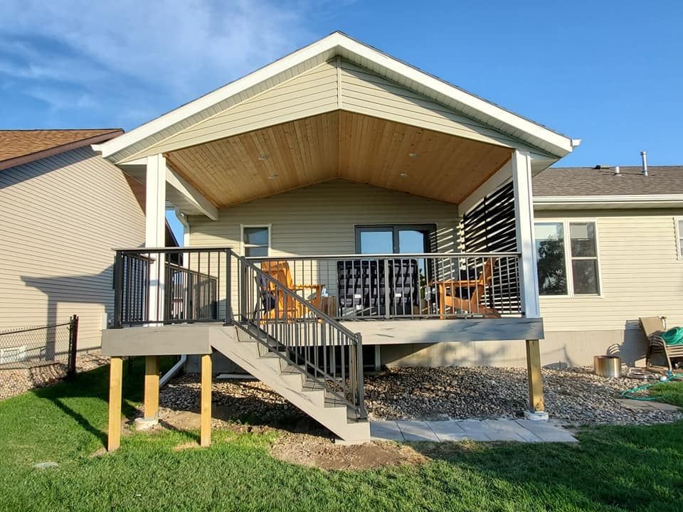 Covered back porch with railing, stairs, and patio furniture on a beige house under a blue sky